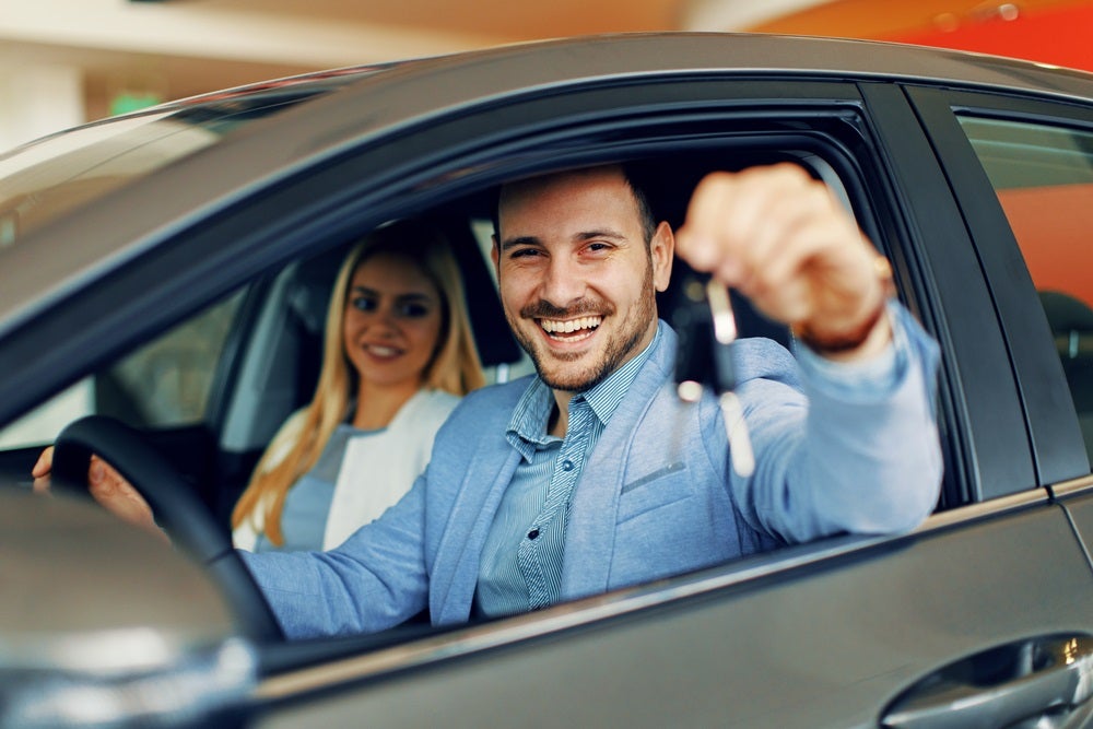 Man behind the wheel of used car showing off keys