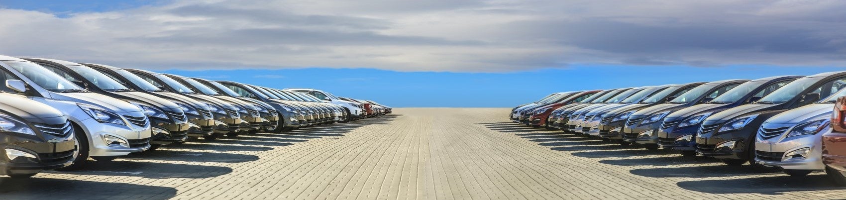 Long lineup of used vehicles in two lines facing each other with blue sky and clouds background